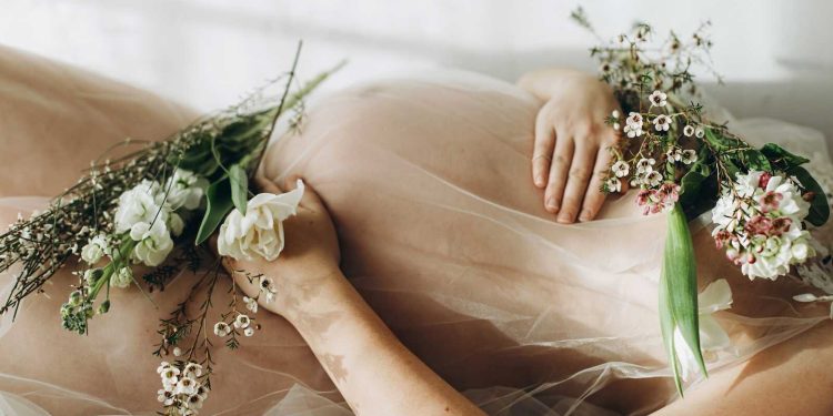 Romantic reclining maternity portrait with sheer fabric and florals for sexy maternity photos.