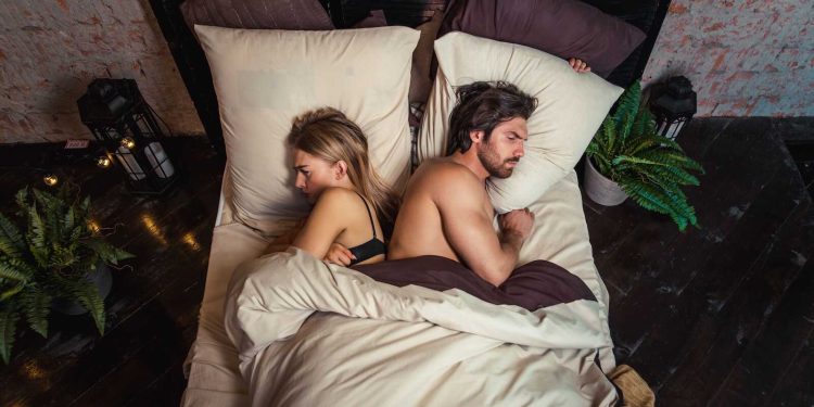 Couple lying back-to-back in bed looking unhappy, illustrating a divorce quiz relationship assessment.