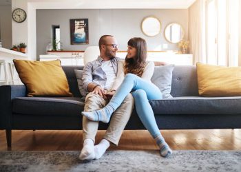 Couple sitting on couch talking and smiling together during marriage communication exercises at home.