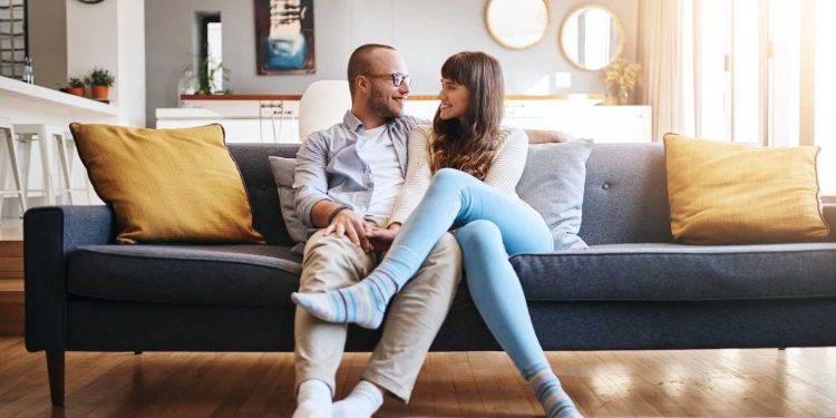 Couple sitting on couch talking and smiling together during marriage communication exercises at home.