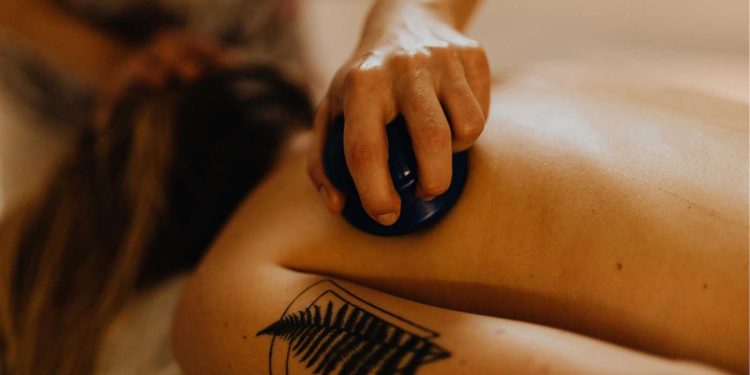 Therapist using a smooth stone during a restorative touch massage on a woman’s back.